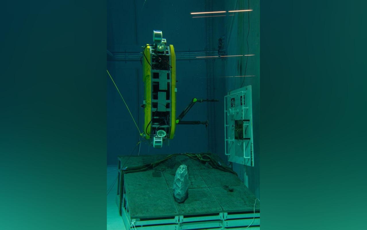 Das AUV führt in aufrechter Position Manipulationsaufgaben an einem Unterwasser-Mockup durch.